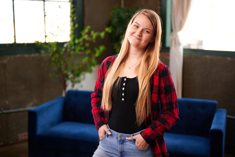 VP of Content, Natalie Nygren, smiles at the camera while standing in front of a blue velvet couch.