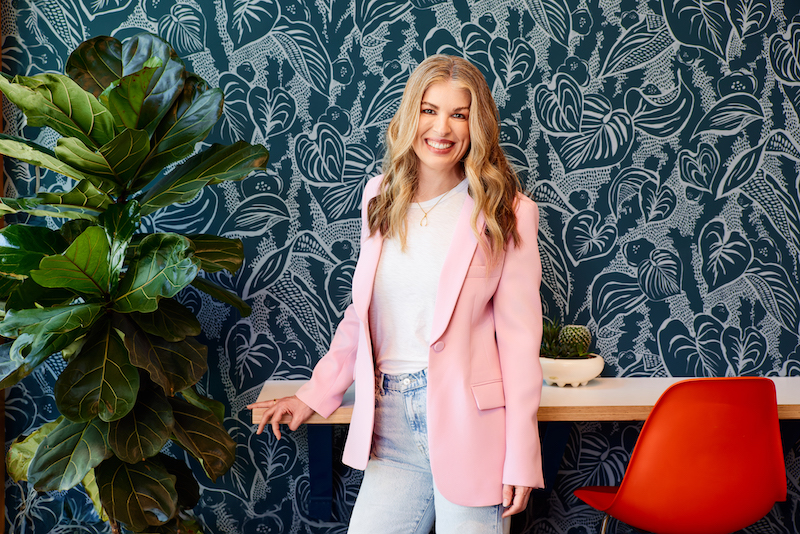Formada Founder and CEO, Meghan Kelly, faces the camera, smiling, while wearing a pink jacket, white shirt, and jeans.