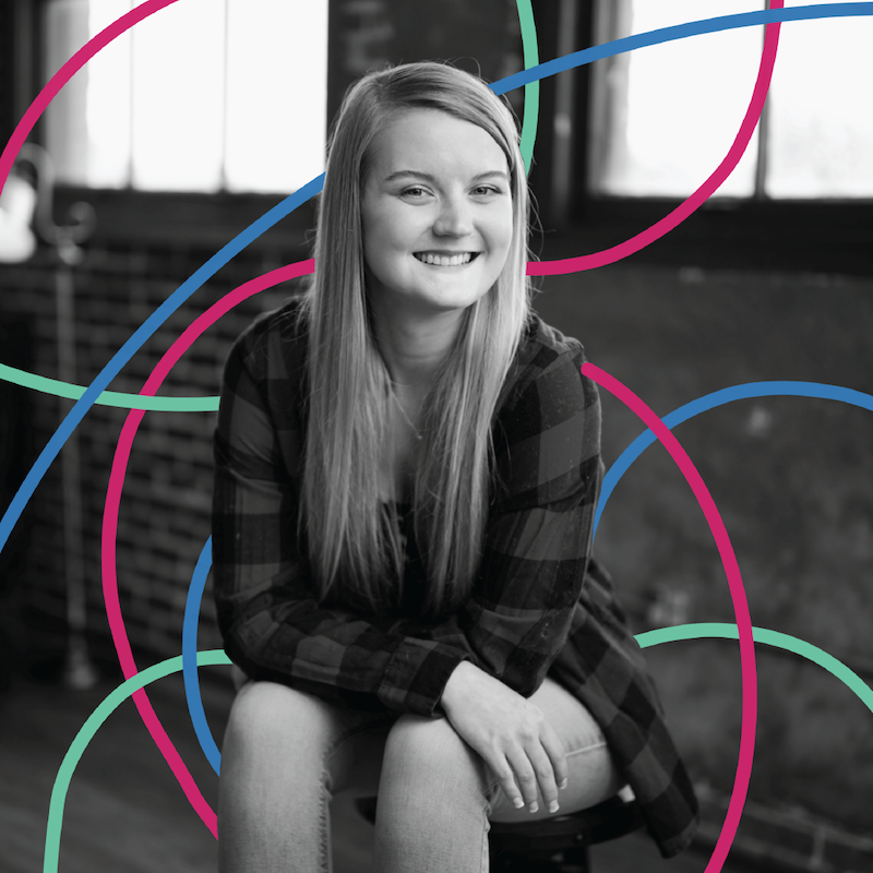 VP of Content, Natalie Nygren, is photographed in black and white, seated in front of the camera and smiling. she is surrounded by teal, magenta, and blue lines, creating a colorful graphic effect.