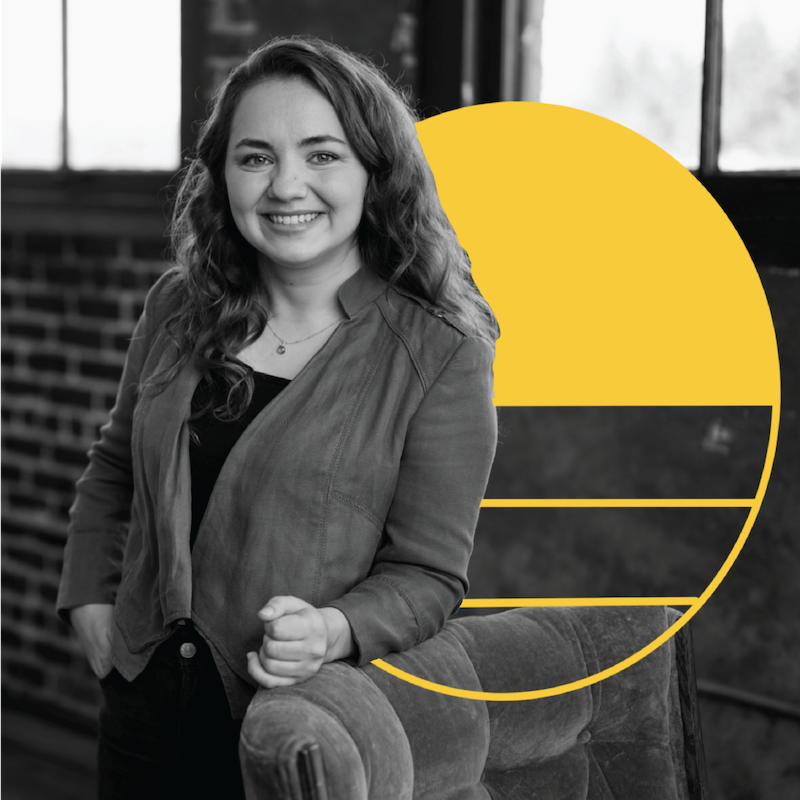 Web Designer Vicki Tolmacheva, shot in black and white, leans against a chair while smiling at the camera. A yellow illustrated circle is drawn just to her right.