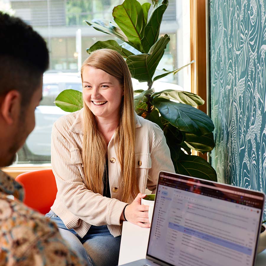 Natalie Bufton, VP of Content at Formada, laughs while talking to Harrison Horblit, VP of Paid Media, while a laptop is open