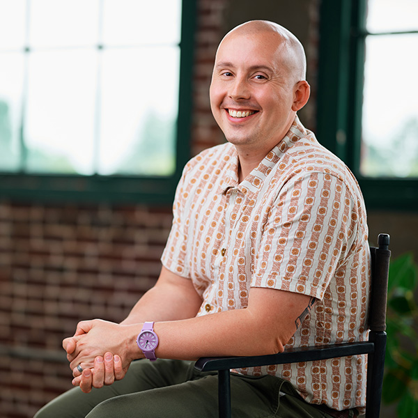 Formada COO and Co-Founder, Garrett Jackson, smiles with his hands held in front of an office brick wall and windows