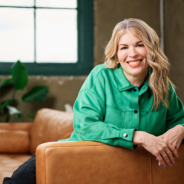 Formada CEO and Co-Founder Meghan Kelly smiles in a green jacket while leaning on a leather couch