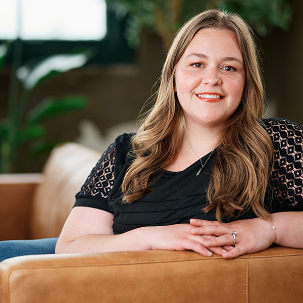 Formada Paid Media Specialist, Ali Russell, smiles while leaning on a leather couch
