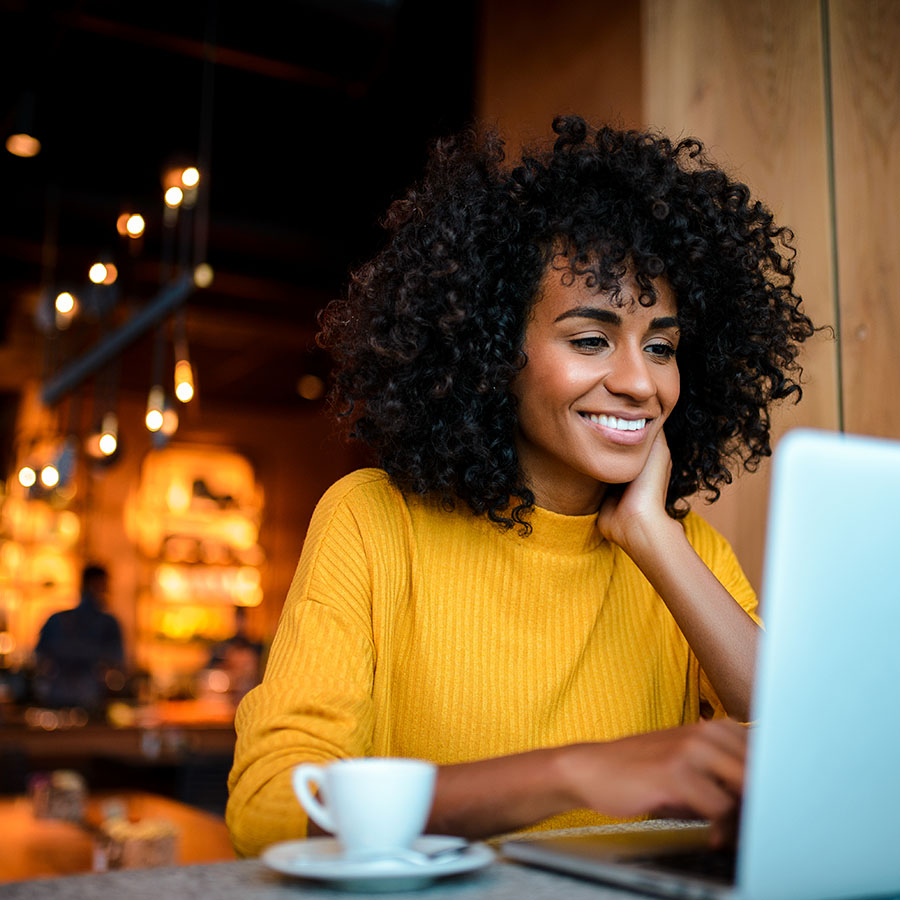 A young woman smiling while on her laptop in a coffee shop