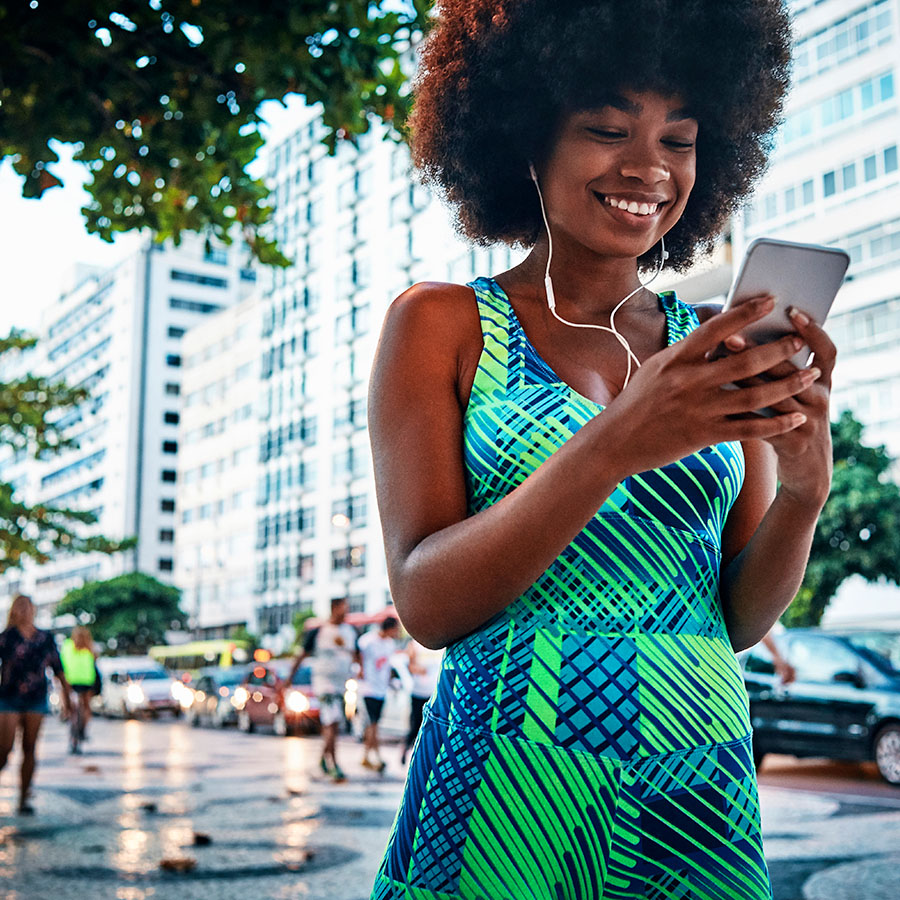 A young woman on a street smiling while looking at her phone