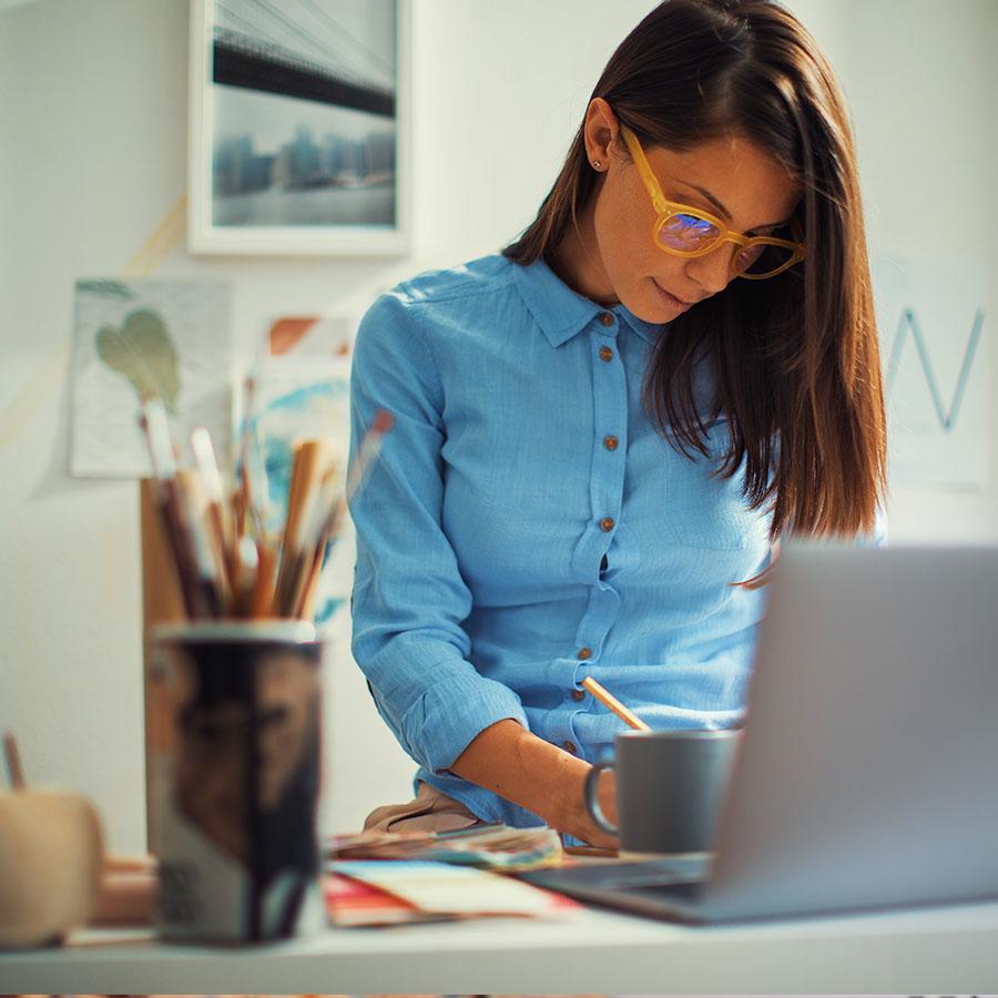 A graphic designer writes some notes down on paper while working on her laptop